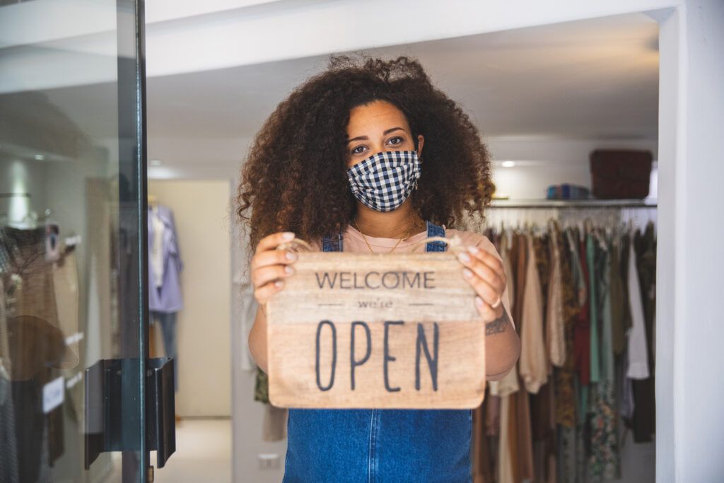 Woman holding Open sign in a small business boutique shop after Covid-19 pandemic